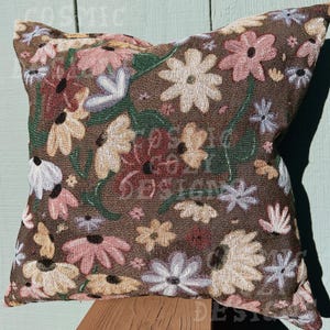 May include: A brown throw pillow with a floral pattern featuring pink, white, and red flowers. The pillow is made of a soft, textured fabric.