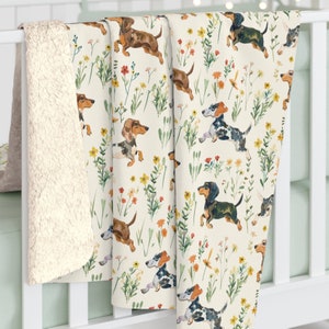 May include: A white and cream throw blanket with a repeating pattern of watercolour dachshunds and flowers. The blanket has a soft, plush texture and is perfect for snuggling up on the sofa.
