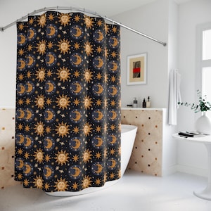 May include: A black shower curtain featuring a repeating pattern of gold and navy blue suns, moons, and stars. The celestial design adds a whimsical touch to any bathroom decor. The curtain is hanging from a curved metal rail.