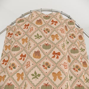 May include: A beige shower curtain with a repeating pattern of pumpkins, bows, sunflowers, and leaves. The design features a grid of squares with a scalloped border and a diamond pattern. The pumpkins are green and orange, and the bows are orange.