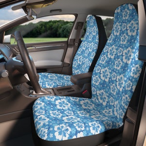 May include: Two blue car seat covers with a white hibiscus flower pattern. The covers are installed in the front seats of a car.