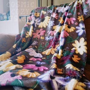 May include: A soft brown fleece throw blanket with a floral pattern featuring yellow, pink, purple, and white flowers on a dark brown background.