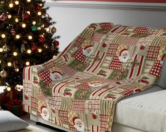 Könnte beinhalten: Eine Weihnachtsdecke mit Patchwork-Design, die den Weihnachtsmann und Weihnachtsbäume zeigt. Die Decke in Rot-, Grün- und Cremetönen ist über ein Sofa drapiert. Im Hintergrund ist ein geschmückter Weihnachtsbaum zu sehen.