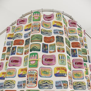 May include: A white shower curtain with a colourful pattern of vintage-style sardine can labels. The labels feature various fish, seafood, and brand names, including "Sardines", "Anchovies", "Ortiz", "Wave Brand", and "Catch Sardines".