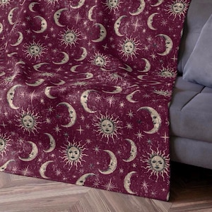 Puede incluir: Una manta de forro polar color burdeos con un patrón celestial vintage que presenta lunas, soles y estrellas.