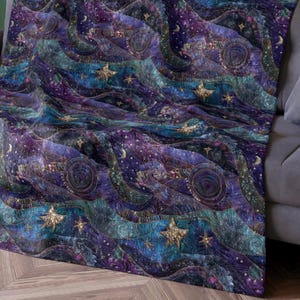 Op de afbeelding: Een hemels thema deken in paars, blauw en teal, met een sterrennacht ontwerp en gouden accenten. De deken heeft een golvend patroon met sterren, manen en cirkelvormige motieven, waardoor een dromerige, kosmische esthetiek ontstaat.
