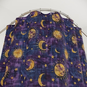 May include: Purple shower curtain featuring a celestial design of suns, moons, and stars. The suns and moons are yellow and gold with a textured appearance. The stars are small and white.