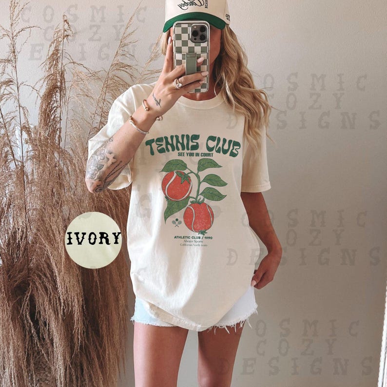 May include: A white oversized t-shirt with a vintage-style graphic of a tennis racket and tomatoes. The text on the shirt reads "Tennis Club" and "See You In Court". The shirt is labeled "Ivory".