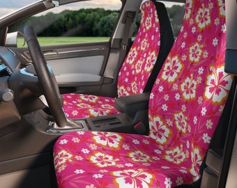 Op de afbeelding: Een paar autostoelhoezen met een felroze achtergrond en een herhalend patroon van grote witte en oranje hibiscusbloemen en kleinere witte bloesems. De hoezen zijn aangebracht over de voorstoelen van een voertuiginterieur.