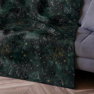 May include: A dark green throw blanket with a scattered gold star pattern. The blanket is draped over a gray couch.