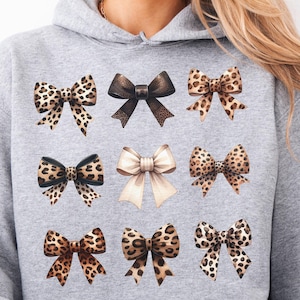May include: A gray hooded sweatshirt with a print of nine different bows. The bows are in various patterns of leopard print, black and white, and beige.