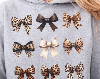 May include: A gray hooded sweatshirt with a print of nine different bows. The bows are in various patterns of leopard print, black and white, and beige.
