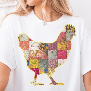 May include: A white t-shirt with a patchwork chicken silhouette design. The chicken is made up of various colorful fabric squares.