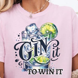 Op de afbeelding: Roze T-shirt met een afbeelding van een gin tonic met de tekst "Gin it to win it".
