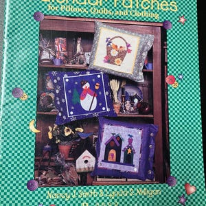 May include: A book titled "Calendar Patches for Pillows, Quilts, and Clothing" by Nancy J. Smith & Lynda S. Milligan. The book cover features a green and white checkered background with a variety of colorful fabric patches depicting different seasons and holidays.