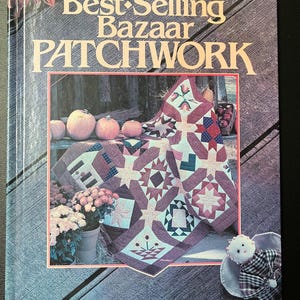 Puede incluir: Un libro titulado "Best-Selling Bazaar Patchwork" que presenta una colcha de retazos colorida con una variedad de patrones y colores. La colcha se muestra sobre una superficie de madera con calabazas y follaje de otoño.