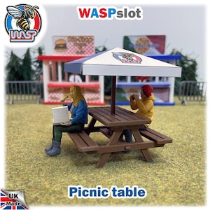 Peut inclure: Une scène de pique-nique miniature avec une table marron, un parasol blanc et bleu, et deux petites figurines. L'une mange, l'autre prend une photo. Le texte "Picnic table" est en bas.