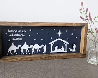 May include: A wooden framed sign with a navy blue background and white silhouette images of the nativity scene and three wise men on camels. The sign reads "Wishing for an old-fashioned Christmas".