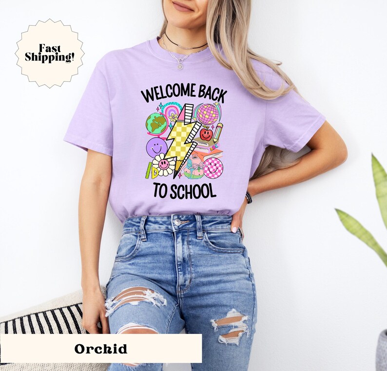 May include: A purple t-shirt with the text "Welcome Back To School" and a graphic of a lightning bolt, a globe, a book, and other school-related items.
