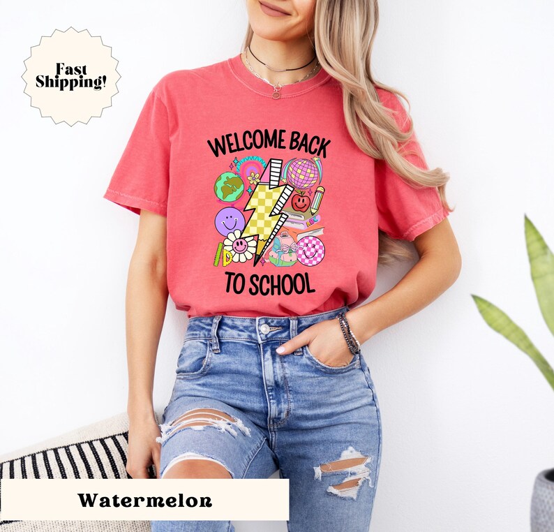 May include: A red t-shirt with a graphic design that says "Welcome Back To School" with a lightning bolt and school-themed icons in pink, yellow, blue, and green.