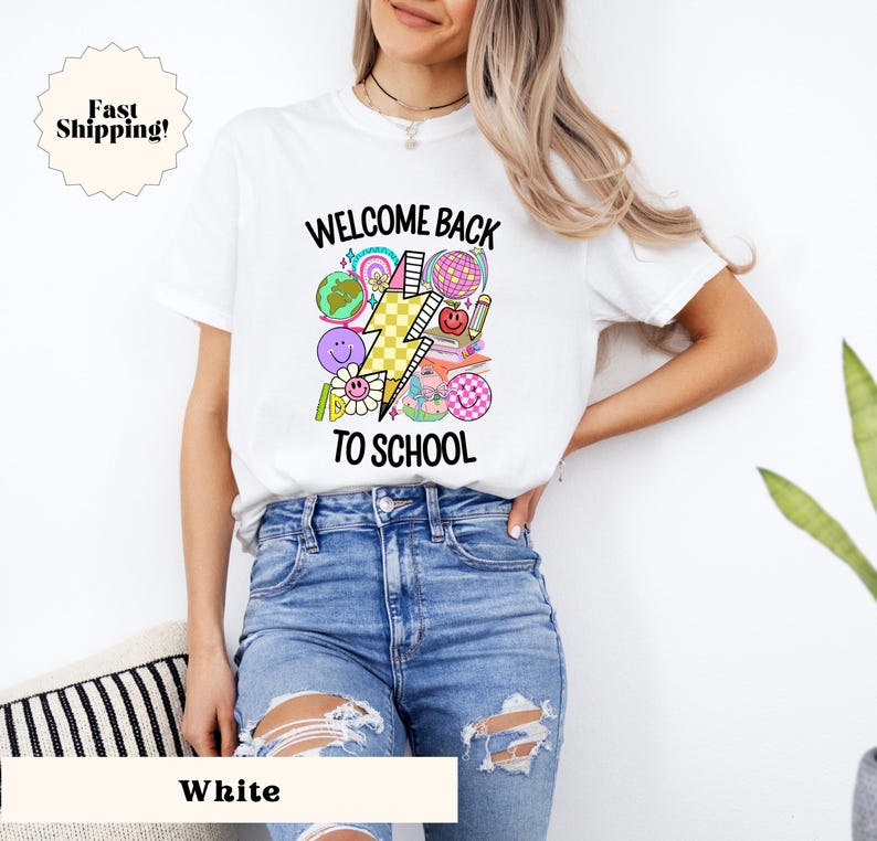 May include: White t-shirt with a graphic design that says "Welcome Back To School" with a lightning bolt and school-themed icons.