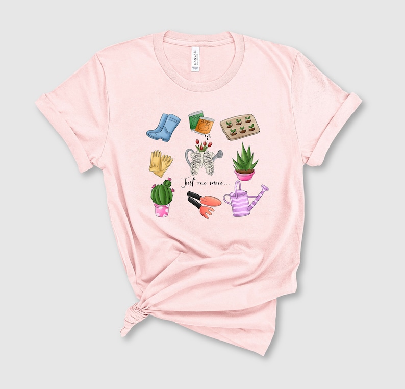 Pu&ograve; includere: Maglietta rosa con un design grafico di attrezzi da giardinaggio e piante. Il testo "Just one more..." &egrave; stampato sulla maglietta.