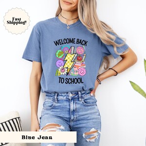 May include: A blue jean t-shirt with the text "Welcome Back To School" and a graphic of a lightning bolt, a globe, a pencil, a book, and a flower.