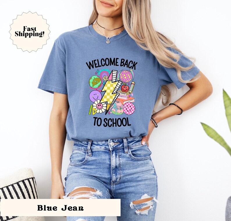 May include: A blue jean t-shirt with the text "Welcome Back To School" and a graphic of a lightning bolt, a globe, a pencil, a book, and a flower.