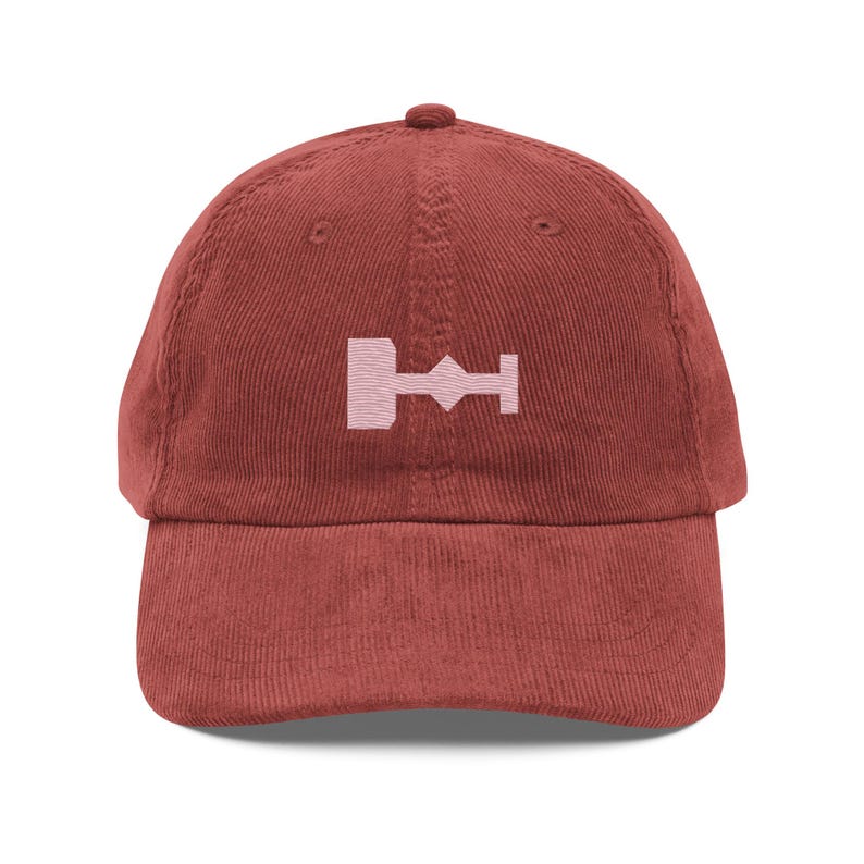 May include: A burgundy corduroy baseball cap with a pink embroidered symbol of a key with a diamond shape in the middle.