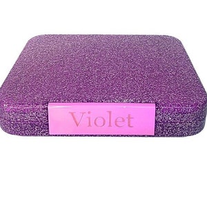 May include: A square, glittery purple box with rounded edges. A pink label on the front reads "Violet". The box is set against a white background.