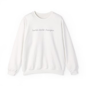 May include: A white crew neck sweatshirt with the text "hurkle-durkle champion" printed in a thin, black font across the chest. The sweatshirt has long sleeves and a relaxed fit.