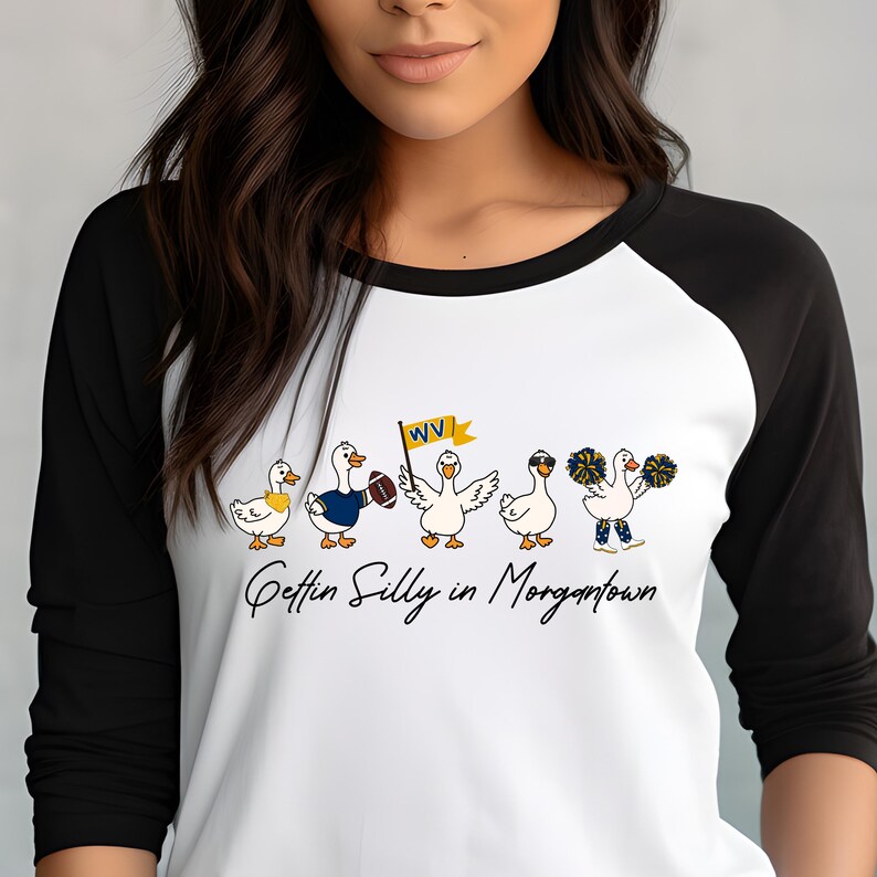 May include: A white raglan shirt with black three-quarter sleeves featuring a graphic of five cartoon ducks. One duck holds a football, another a yellow WV flag, and one wears sunglasses. The text below reads Gettin Silly in Morgantown.