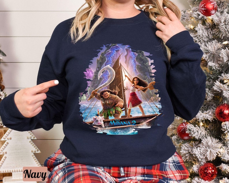 May include: Navy blue sweatshirt featuring a graphic of Moana and Maui from the film Moana 2. The graphic depicts them sailing on a boat with a pig and a rooster.