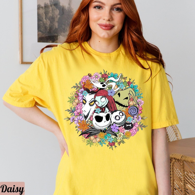 K&ouml;nnte beinhalten: Gelbes T-Shirt mit einem bunten Grafikdruck von Figuren aus dem Film Nightmare Before Christmas. Die Figuren sind von Blumen umgeben.