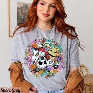 K&ouml;nnte beinhalten: Ein graues T-Shirt mit einem bunten Blumenmuster, das Figuren aus dem Film "Nightmare Before Christmas" zeigt. Die Figuren sind Jack Skellington, Sally und Oogie Boogie.