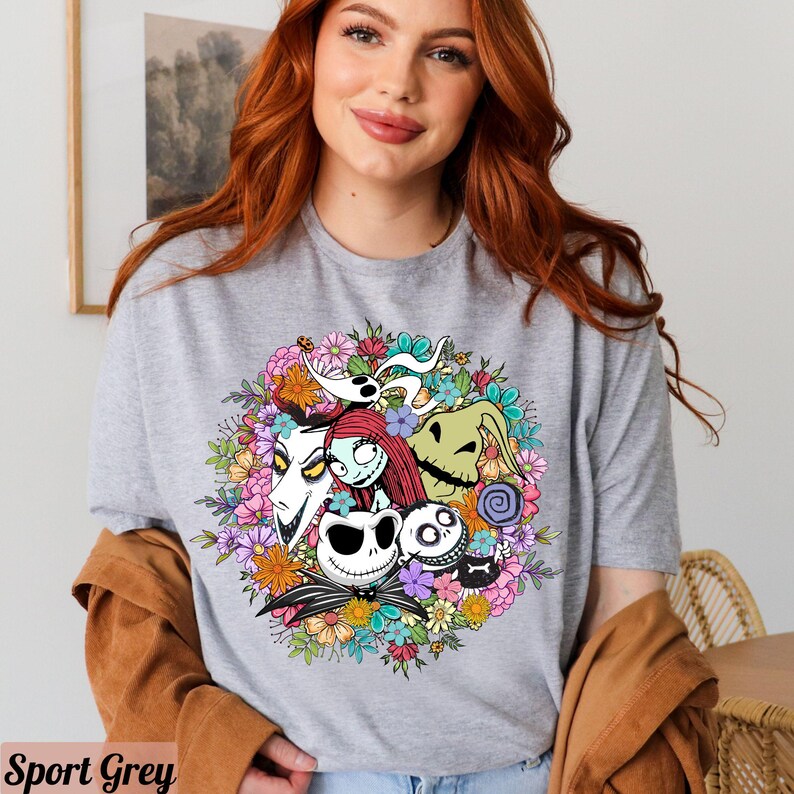K&ouml;nnte beinhalten: Ein graues T-Shirt mit einem bunten Blumenmuster, das Figuren aus dem Film "Nightmare Before Christmas" zeigt. Die Figuren sind Jack Skellington, Sally und Oogie Boogie.