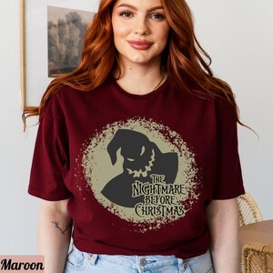 Puede incluir: Una camiseta de color granate con un gr&aacute;fico circular beige desgastado que presenta una silueta negra de Jack Skellington de la pel&iacute;cula "Pesadilla antes de Navidad". El texto "The Nightmare Before Christmas" est&aacute; impreso en negro dentro del c&iacute;rculo.