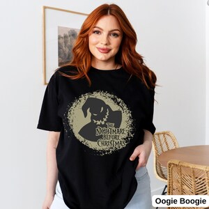 Puede incluir: Una camiseta negra con un gr&aacute;fico circular desgastado de Oogie Boogie de "Pesadilla antes de Navidad". El gr&aacute;fico es de color marr&oacute;n claro y presenta el texto "The Nightmare Before Christmas".