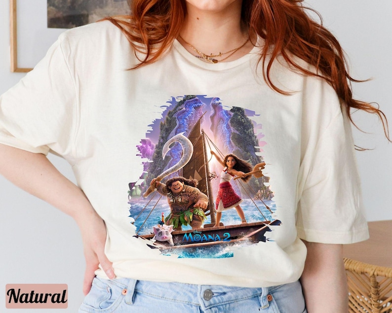 May include: A white t-shirt featuring a colourful graphic of Moana and Maui sailing on a boat. The graphic includes the text "Moana 2".