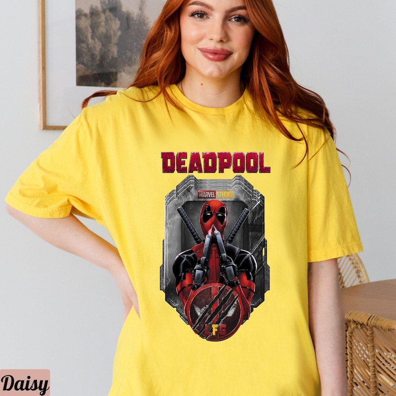 May include: Yellow t-shirt with a graphic of Deadpool from Marvel Studios. The graphic shows Deadpool in a red and black suit with his hands up in a fighting pose. The text "DEADPOOL" is printed in red above the graphic.