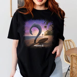 May include: Black t-shirt with a graphic print of a sunset scene with a hook and a paddle. The text "Moana 2" is printed below the graphic.