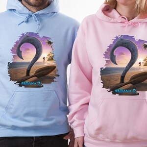 Puede incluir: Dos sudaderas con capucha con un estampado gr&aacute;fico de un gancho y una pala de dibujos animados de la pel&iacute;cula Moana 2. La sudadera de la izquierda es azul claro y la sudadera de la derecha es rosa.