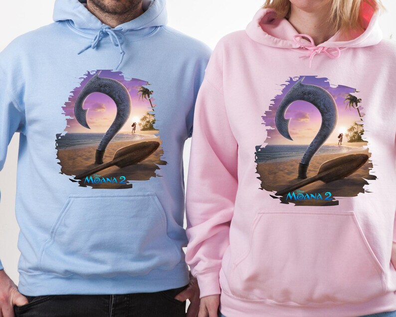 Puede incluir: Dos sudaderas con capucha con un estampado gr&aacute;fico de un gancho y una pala de dibujos animados de la pel&iacute;cula Moana 2. La sudadera de la izquierda es azul claro y la sudadera de la derecha es rosa.