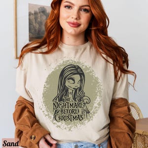 Puede incluir: Una camiseta beige claro con un estampado gr&aacute;fico desgastado de Sally de la pel&iacute;cula "Pesadilla antes de Navidad". El gr&aacute;fico incluye el texto "The Nightmare Before Christmas".