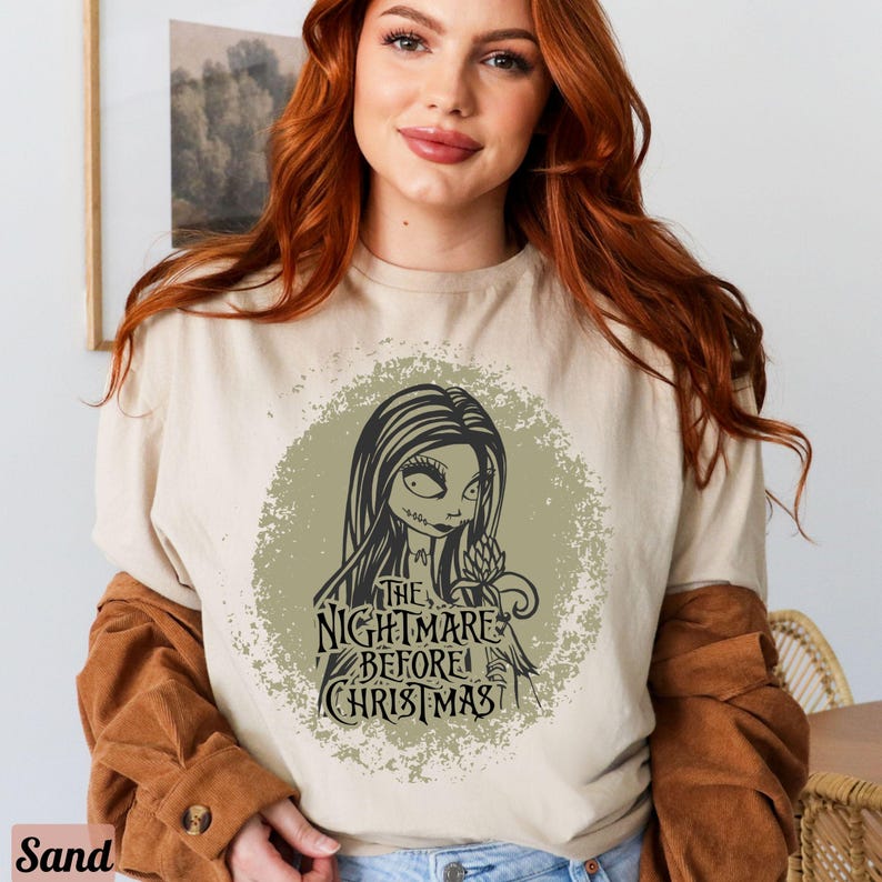 Puede incluir: Una camiseta beige claro con un estampado gr&aacute;fico desgastado de Sally de la pel&iacute;cula "Pesadilla antes de Navidad". El gr&aacute;fico incluye el texto "The Nightmare Before Christmas".