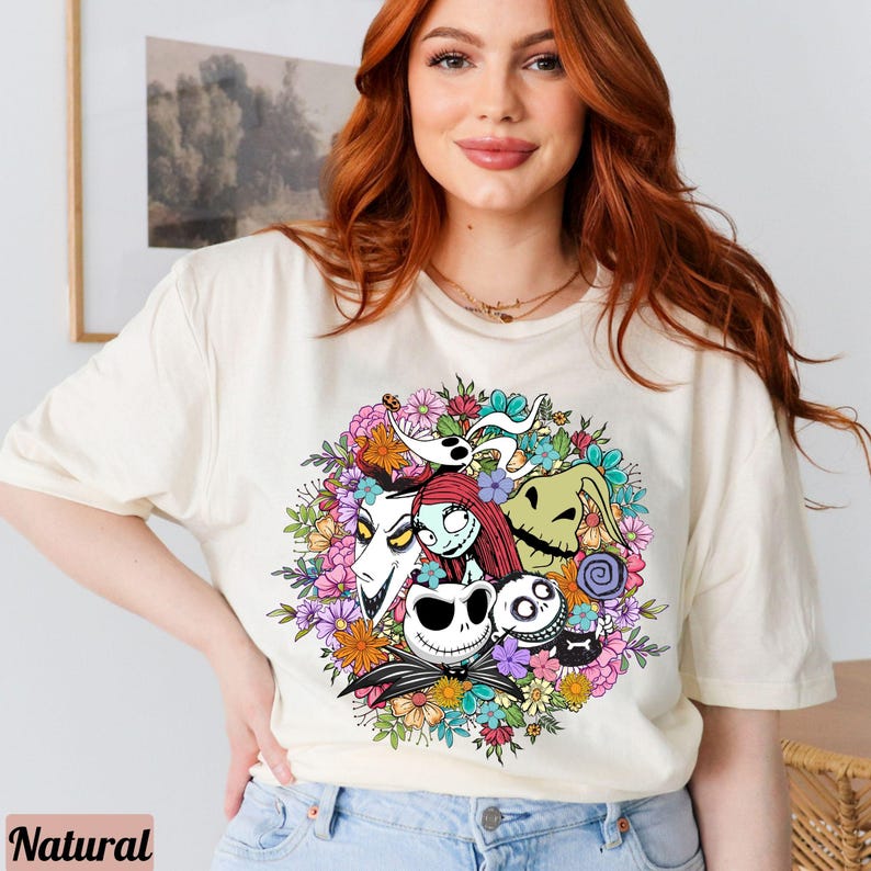 K&ouml;nnte beinhalten: Ein wei&szlig;es T-Shirt mit einem bunten Grafikdruck von Figuren aus dem Film Nightmare Before Christmas. Die Figuren sind von Blumen und Bl&auml;ttern umgeben.