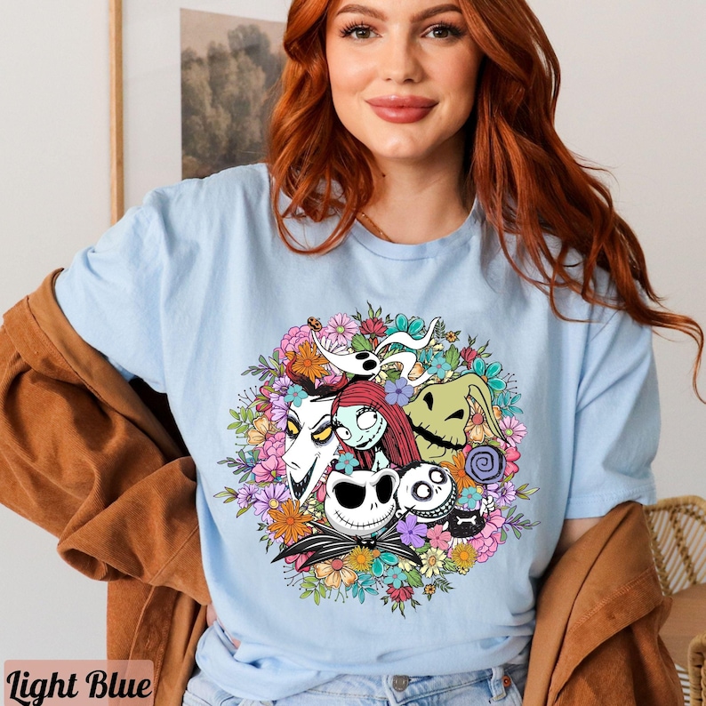 K&ouml;nnte beinhalten: Hellblaues T-Shirt mit einem bunten Blumenkranz-Design mit Figuren aus dem Film Nightmare Before Christmas. Die Figuren sind Jack Skellington, Sally, Zero und Oogie Boogie.