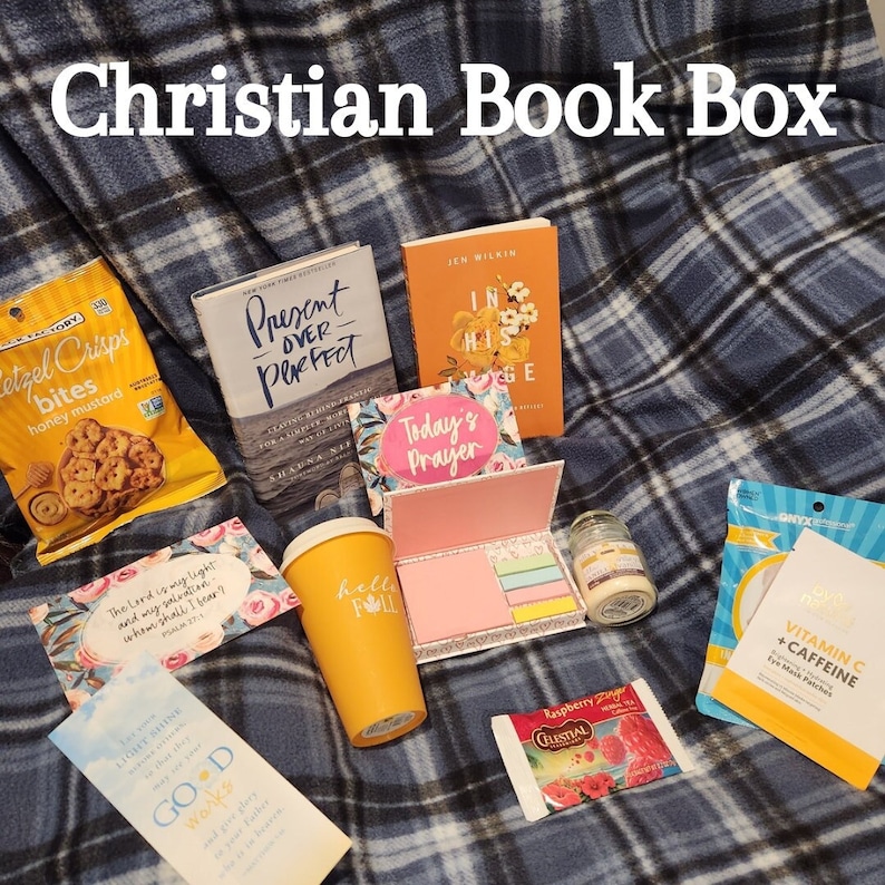 May include: A Christian Book Box subscription box with a variety of items, including two books, a pink and white prayer journal, a yellow coffee mug, a candle, a pack of tea, a bag of pretzels, and a pack of vitamin C and caffeine eye patches.