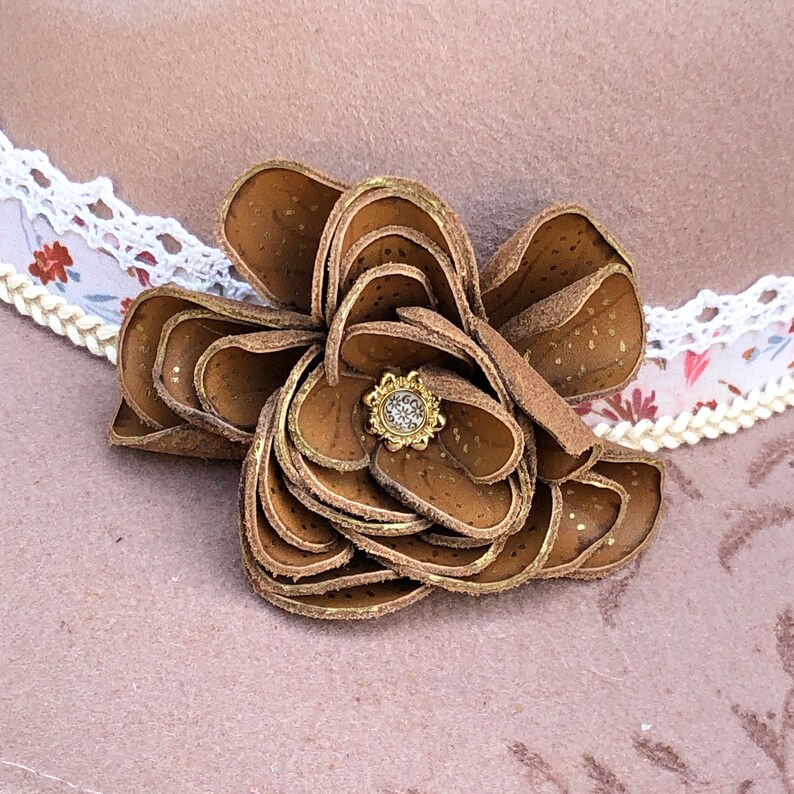 以下が含まれることがあります： 金色のセンターを持つ茶色の革の花。花は複数の革の層でできており、表面にテクスチャがあります。