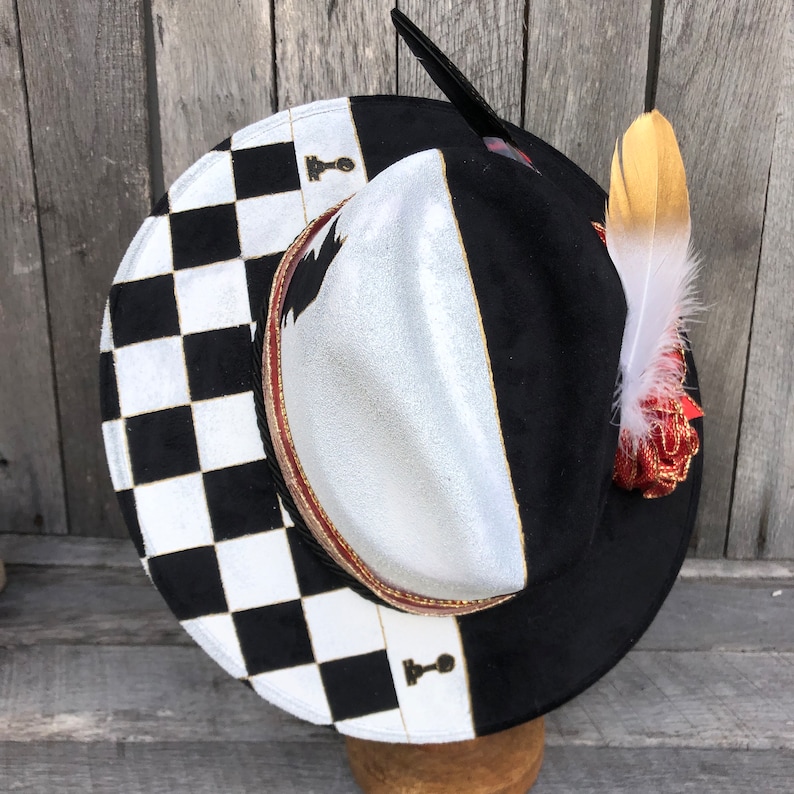 May include: A black and white checkered fedora hat with a silver and black crown. The hat has a gold trim and a gold feather accent.